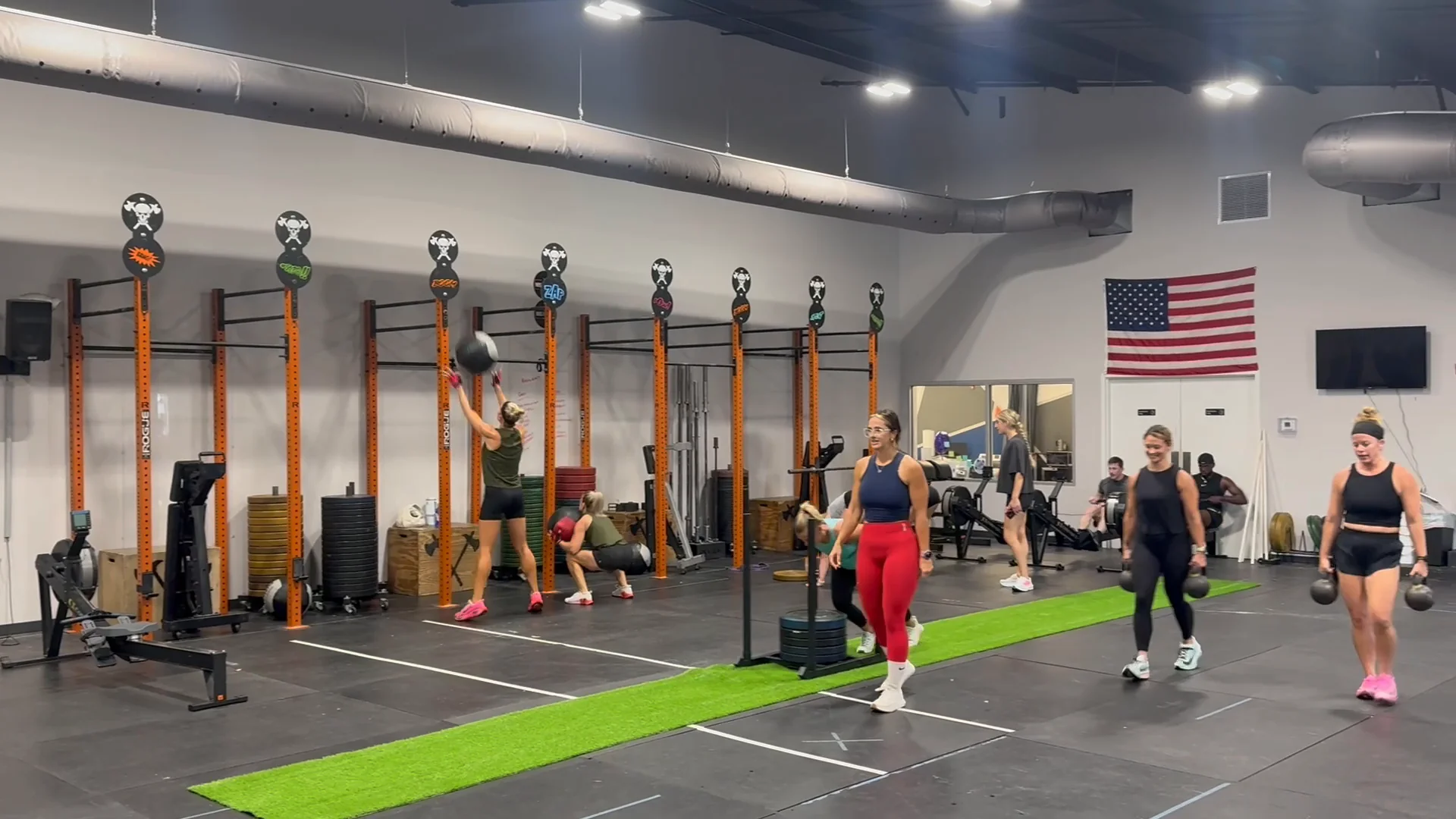 A full HYROX class training across the Bluff City Performance floor, with wall balls at the orange rig and kettlebell carries on the turf lane